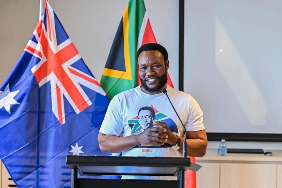 Lovemore Ndou speaking at a lectern in front of the Australian and South African flags