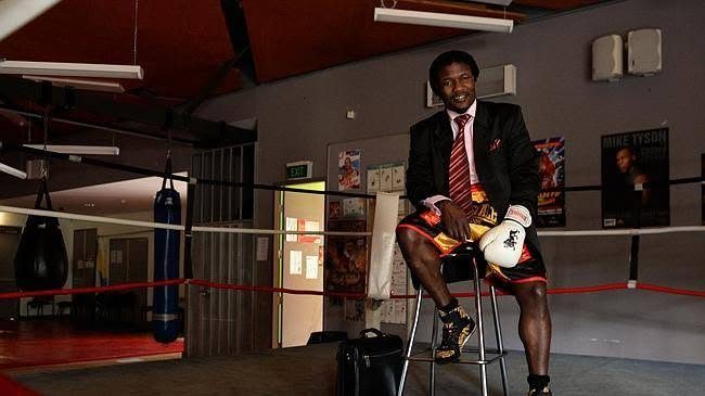 Lovemore Ndou seated in a boxing ring wearing a suit jacket and boxing shorts